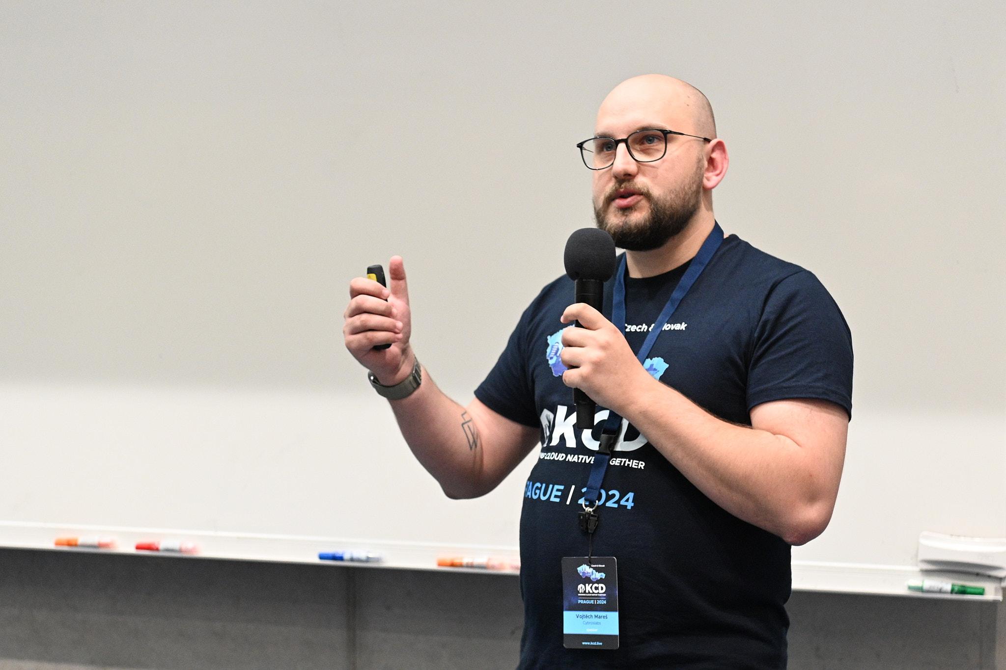 Vojtěch Mareš s mikrofonem, přednášející o CloudNativePG